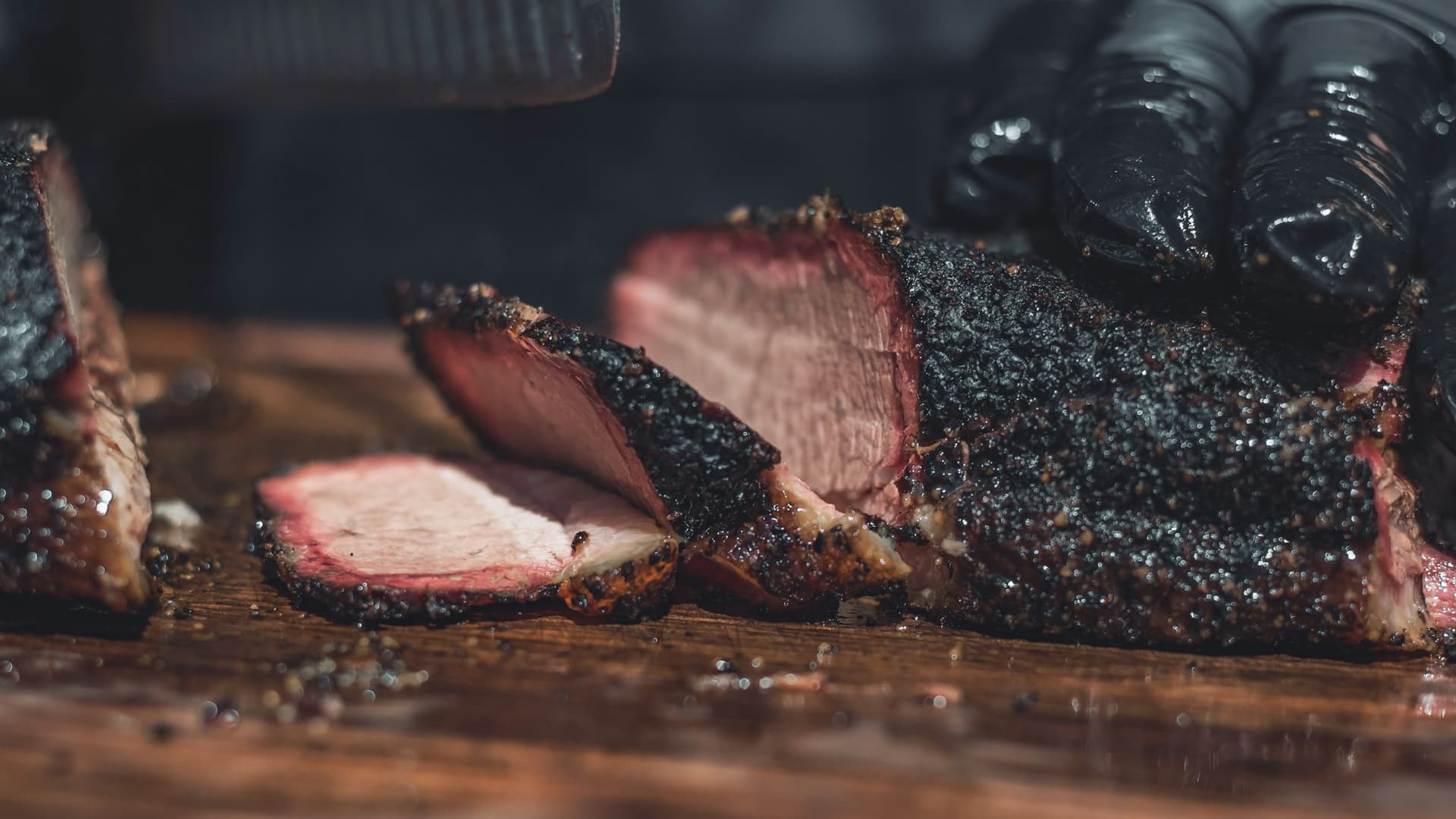 Whole peppered brisket on the block at Emberline, one slice down, pit room dark behind it