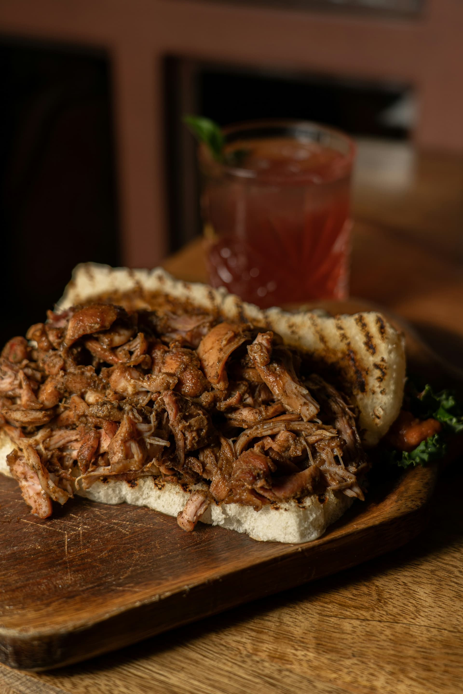 Open-faced smoked pork on grilled bread with a hibiscus lemonade behind